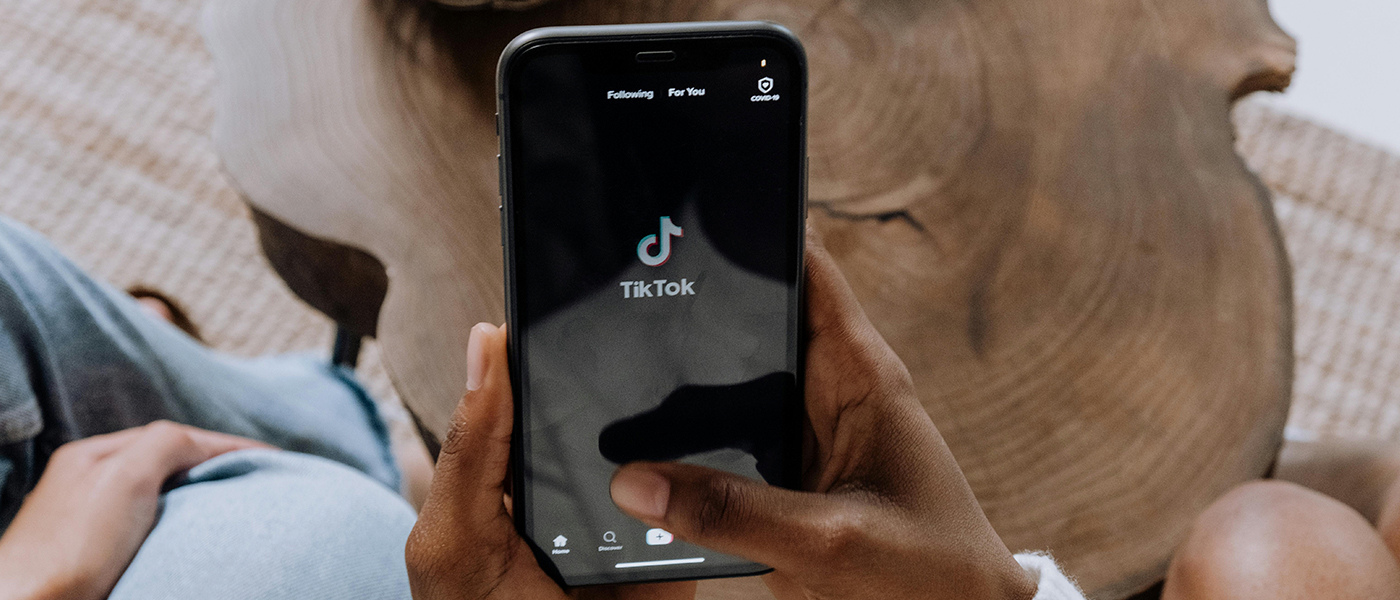 Hände die ein Handy halten, auf dem das Logo von TikTok zu sehen ist.